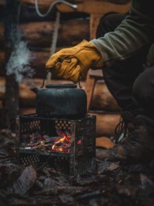 Gros plan d'une bouilloire sur un réchaud de camping avec une main recouverte d'un gant qui l'ajuste à l'extérieur.