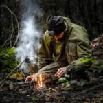 Un homme s'agenouille dans une forêt tout en allumant habilement un feu de camp, mettant en valeur ses compétences de survie.