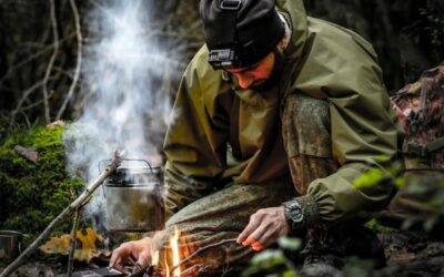 Un homme s'agenouille dans une forêt tout en allumant habilement un feu de camp, mettant en valeur ses compétences de survie.