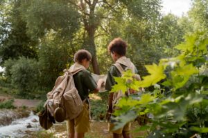 Deux jeunes scouts en uniformes explorant une forêt avec une carte au bord d'un ruisseau.