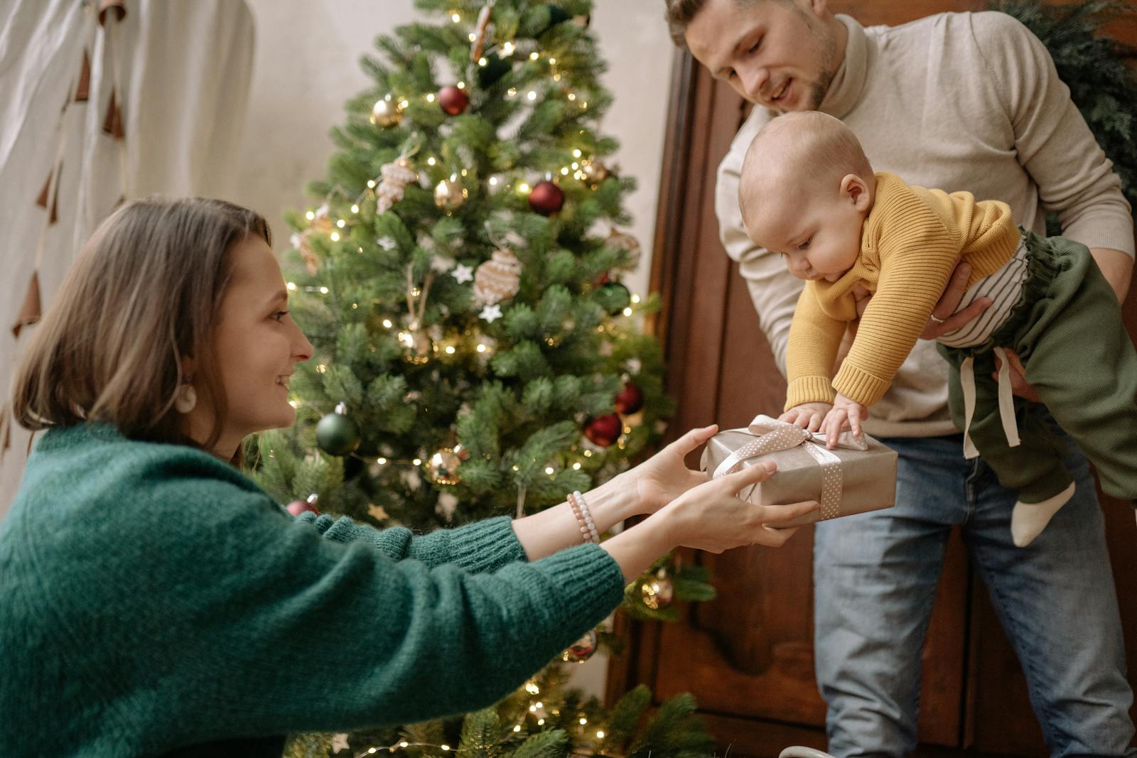 Un moment de joie en famille avec les parents échangeant un cadeau avec leur bébé près du sapin de Noël.
